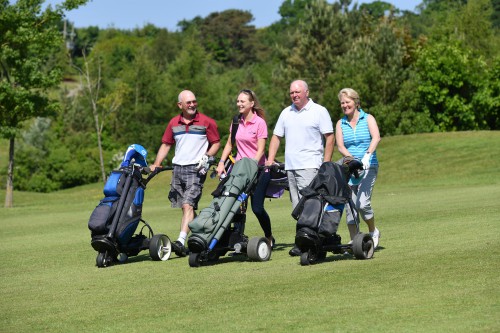 Two men and two women wheeling three golf bags on golf course